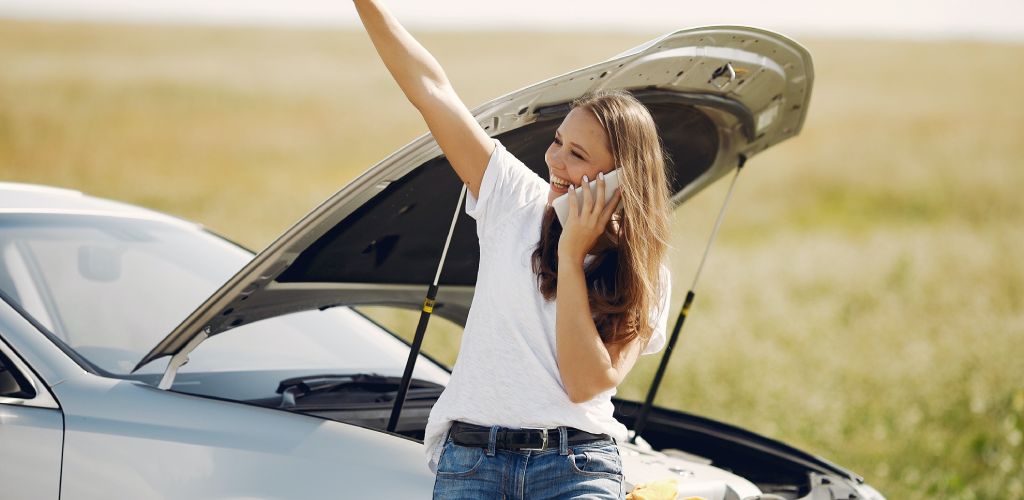 woman sitting on her broken down car waiting for a tow truck