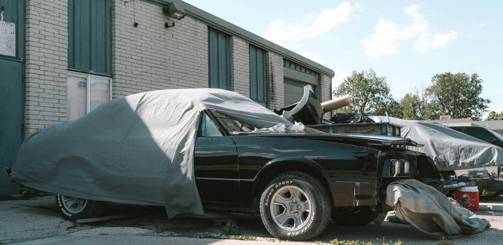 a damaged, unregistered car sitting behind a shed